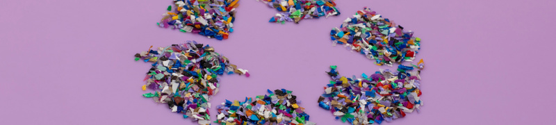 Symbol für Recycling aus buntem Kunststoffgranulat auf einem lila Hintergrund