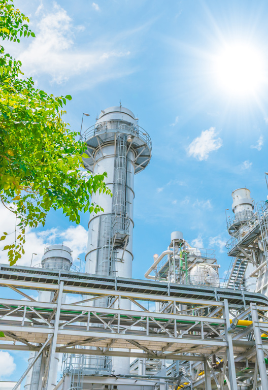 Modernes Konzept für eine nachhaltige Energiewirtschaft. Kraftwerk unter blauem Himmel hinter einem Baum.