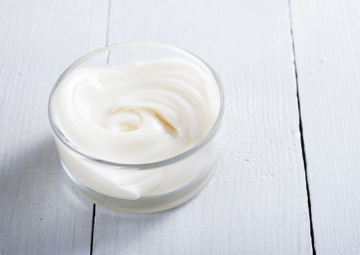 offener Tiegel mit weißer Creme auf hellem Holztisch